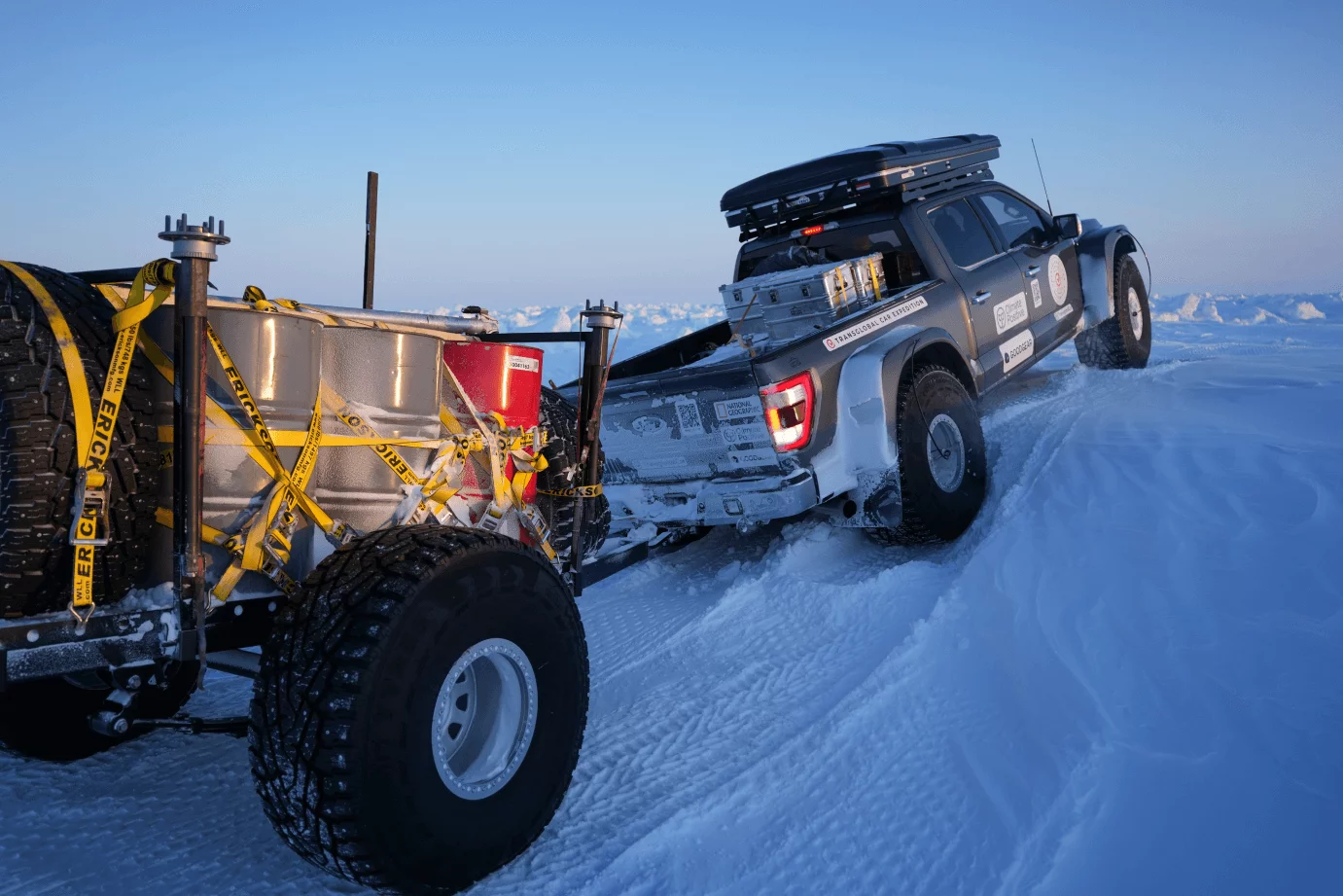 A truck hauls a loaded trailer uphill in the snow.
